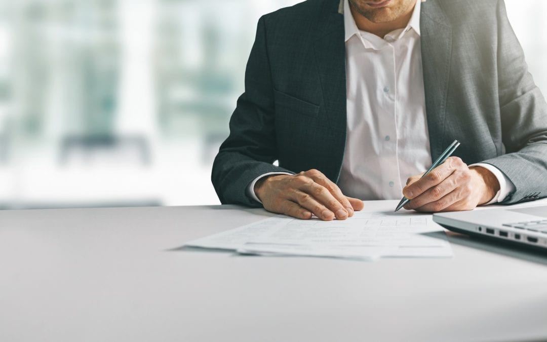 young man in suit writing business papers at desk in modern coworking office. copy space